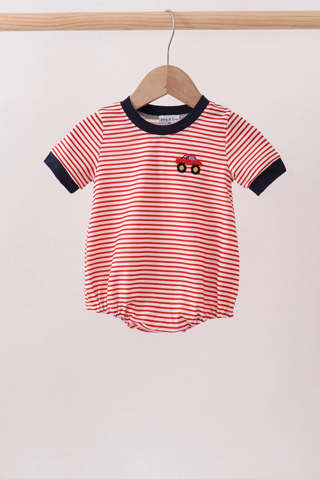 Red and white striped baby romper with a car design on a hanger against a light background