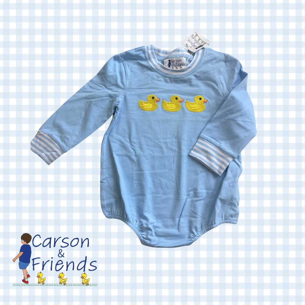 A light blue long-sleeve baby bodysuit with three yellow rubber duck graphics on the chest and striped cuffs, displayed on a white and light blue gingham background with a 'Carson & Friends' logo in the bottom left corner.
