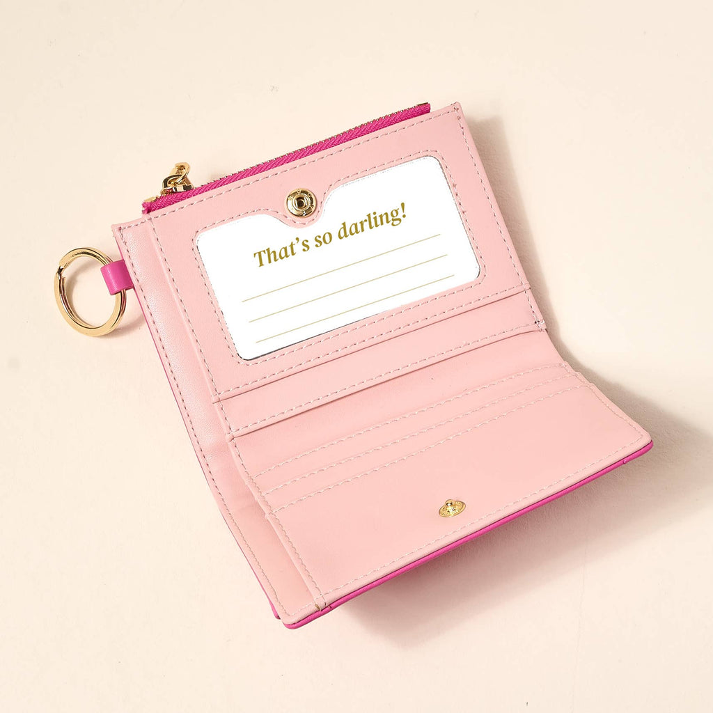 Pink wallet with a keychain and 'That's so darling!' card on a beige background